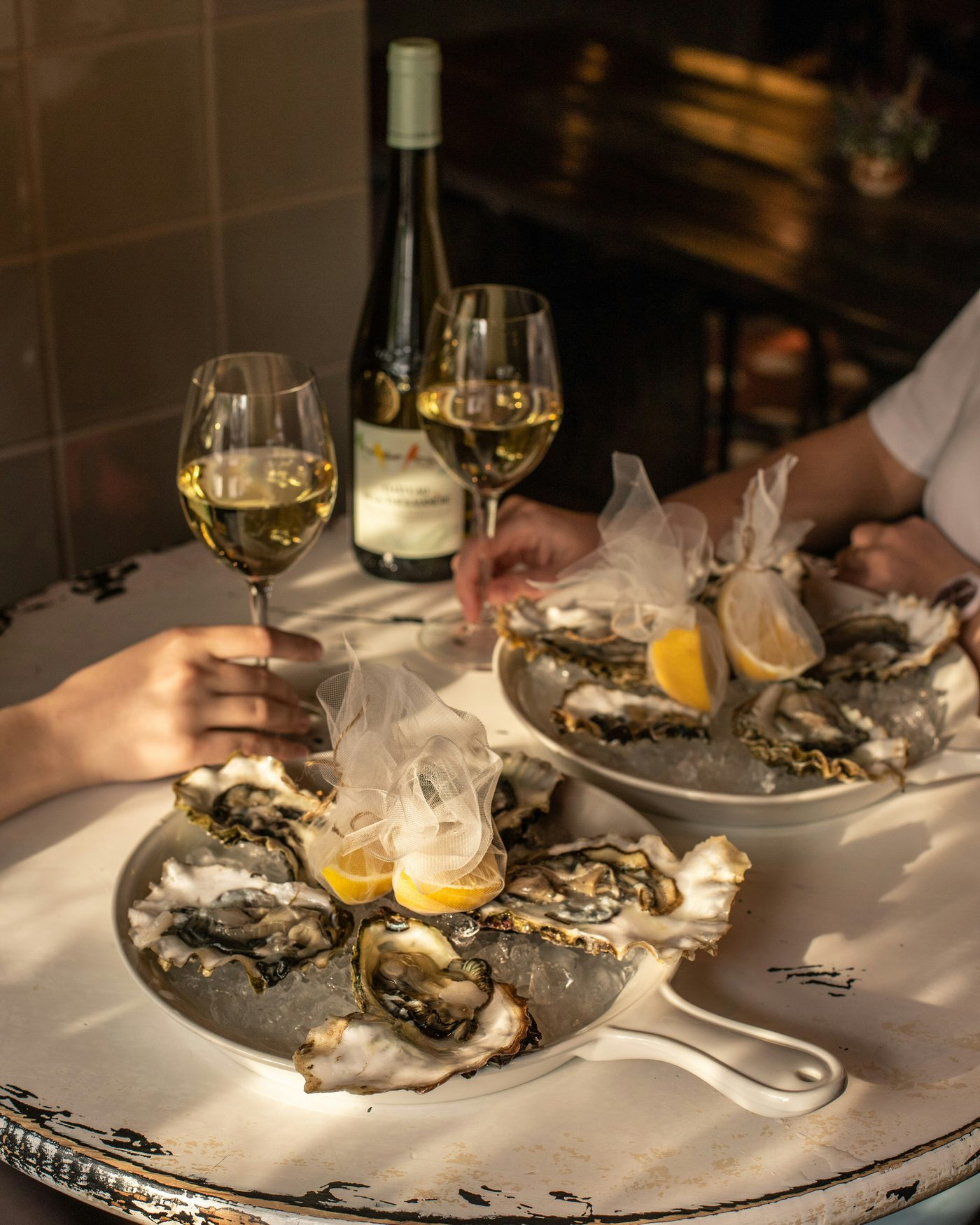 Platters of fresh oysters on ice beside two glasses of chilled white wine