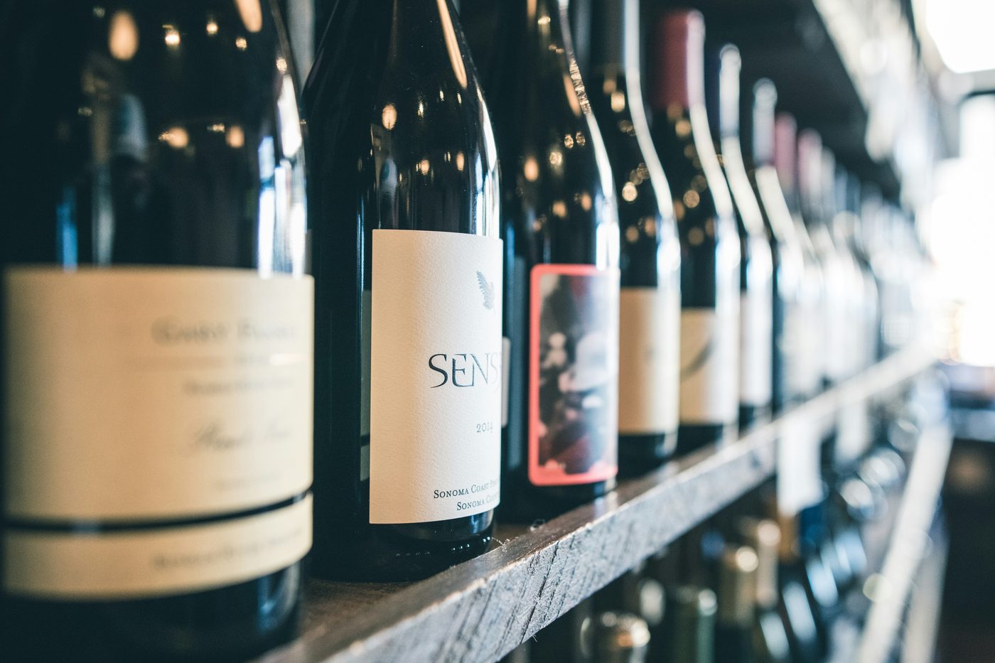 A row of wine bottles resting on a wooden shelf